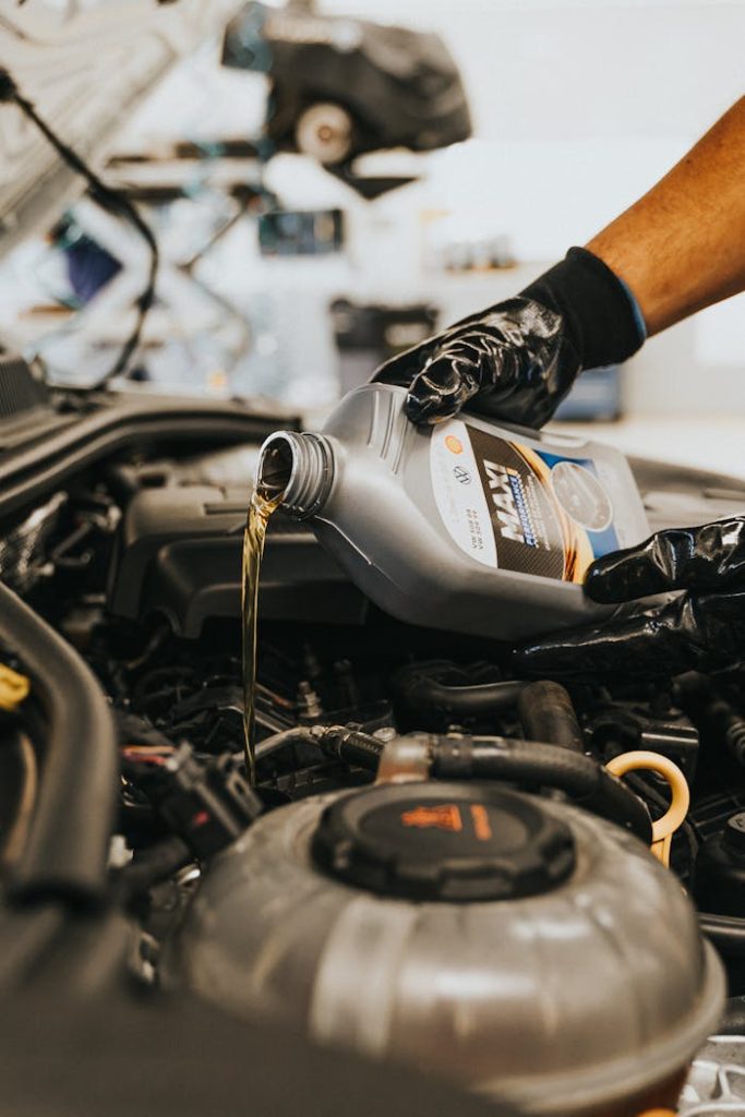 hands-pouring-oil-to-engine-13065694 A close-up of a mechanic in gloves pouring engine oil into a car engine, showcasing automotive maintenance.