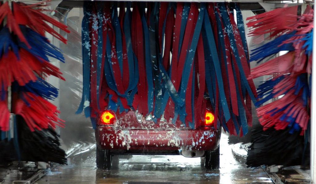 zipwp-image-210627 Red car being cleaned in an automated car wash with colorful brushes and soap suds.